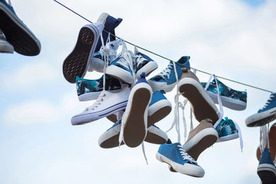 Low angle view of shoes tied on cable against blue sky