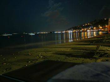 Illuminated city by sea against sky at night