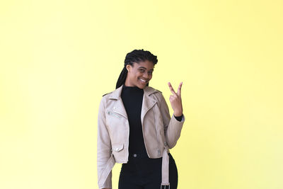 Young woman standing against yellow background