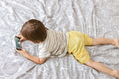 A cute boy, toddler, lies on the bed in the bedroom and plays with the phone, smartphone. 