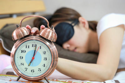 Close-up of alarm clock against woman sleeping on bed