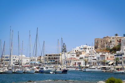 Sailboats in city by sea against clear sky