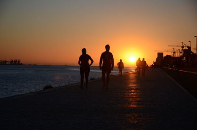 Silhouette people on beach against sky during sunset