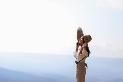 Side view of smiling woman wearing hat by mountains against sky