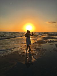 Silhouette man standing on beach against sky during sunset