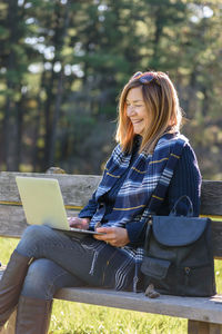 Mature woman using laptop while sitting on bench in park