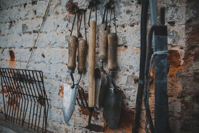 Close-up of gardening equipment hanging by weathered wall