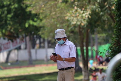 Man holding mobile phone while standing by plants