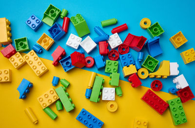 Scattered parts of a plastic children's designer, top view. yellow blue background