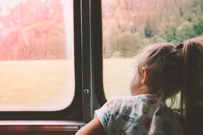 Rear view of girl looking through window while traveling in train