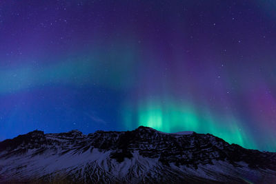 Low angle view of aurora borealis over snowcapped mountains at night