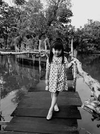 Full length portrait of girl standing on footbridge over lake