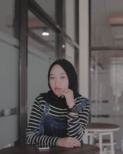 Portrait of teenage girl sitting on seat by table