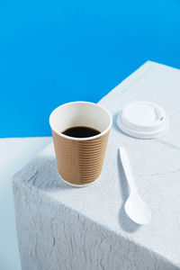 Reusable cup with coffee on white table with white plastic cap and spo