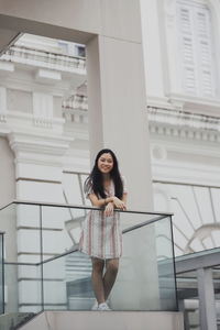 Portrait of young woman standing by railing against building 