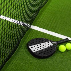 Closeup view of  paddle racket and balls in a padel tennis court near the net green with white lines