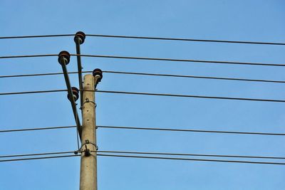 Low angle view of bird perching on electricity pylon against blue sky