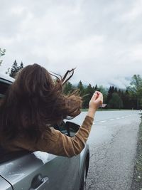 Rear view of woman looking through car window on road