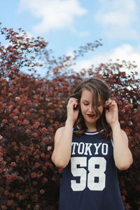 Young woman standing by tree against sky