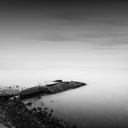 Pier at beach against sky during foggy weather