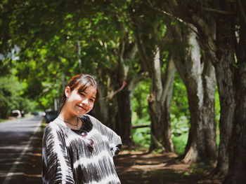 Portrait of smiling young woman standing against trees