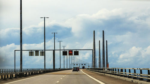 Cars on bridge against cloudy sky