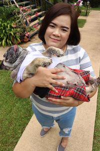 High angle portrait of mid adult woman carrying pug while standing on footpath in park