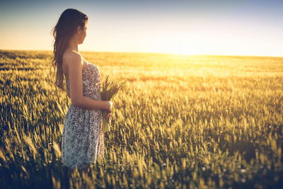 Side view of woman standing amidst plants on field during sunset
