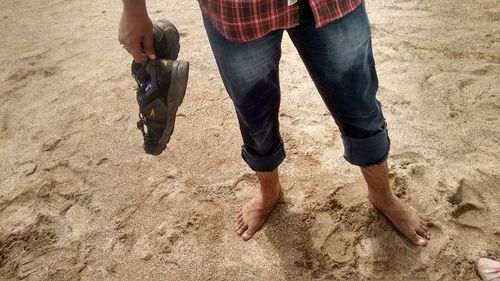 Low section of man with shoes standing on sandy beach