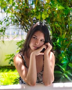 Thoughtful young woman looking away while sitting at table against plants