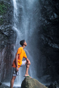 Man standing on rock against waterfall