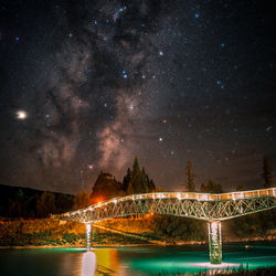 Illuminated bridge over river against sky at night