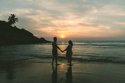 Silhouette couple on beach against sky during sunset