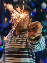 Close-up of boy holding burning sparkler at night