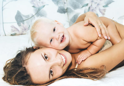 Portrait of mother with naked daughter lying on bed at home