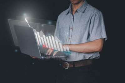 Midsection of man using mobile phone against black background
