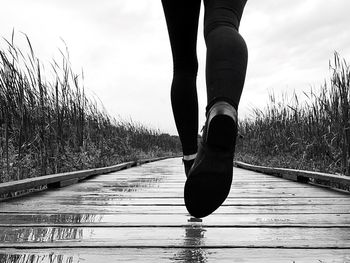 Low section of woman standing in wet boardwalk against sky