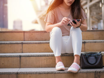 Midsection of woman using mobile phone while sitting on staircase