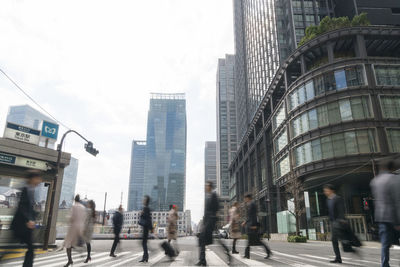 People walking on road amidst buildings in city against sky