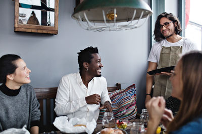 Happy friends looking at young waiter while enjoying brunch in restaurant