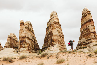 Hiker with backpack walks next to red sandstone towers in utah desert