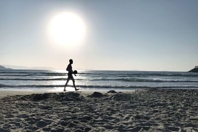 Silhouette man walking on beach against clear sky