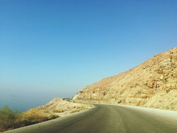 Empty road leading towards mountains against blue sky
