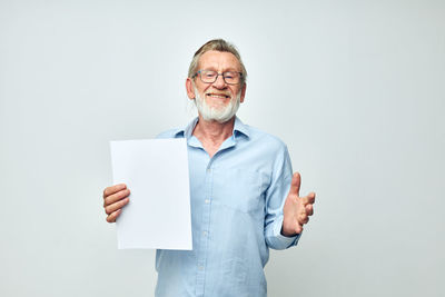 Portrait of smiling young woman holding book while standing against white background