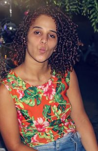 Portrait of beautiful young woman protruding while standing outdoors at night