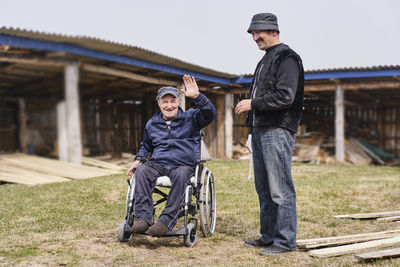 A happy senior man  in a wheelchair in the yard smiling. his friend  next to him.