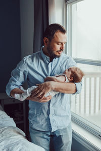 Father carrying baby daughter while standing at home