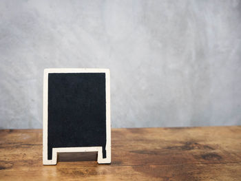 Close-up of blank black placard on wooden table against wall