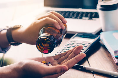 Cropped hands taking pills at desk in office