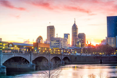 Arch bridge over river and buildings against sky during sunset